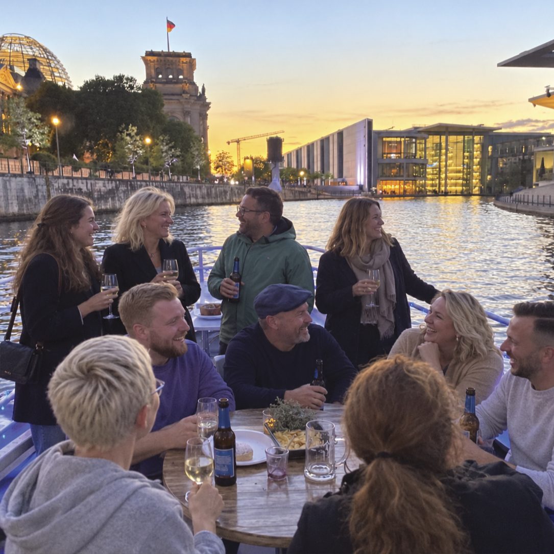 Gäste sitzen in der Abendsonne an Deck zusammen, im Hintergrund Reichstagsgebäude und Regierungsviertel